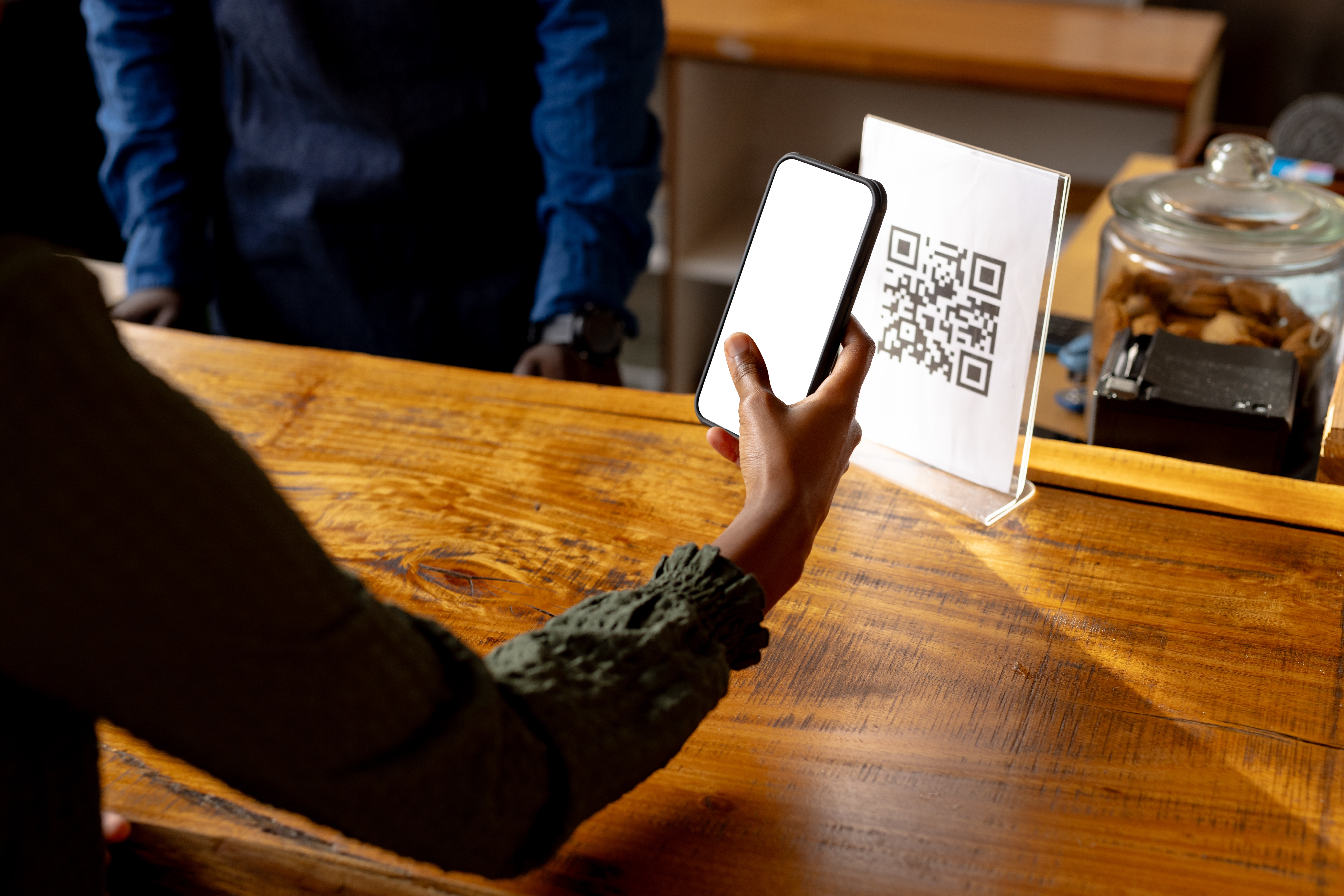 Customer scanning a QR code printed paper with a smartphone at a checkout counter.