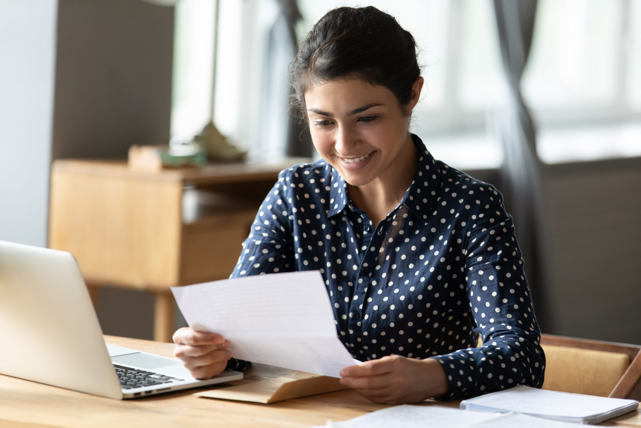 Smiling woman reading mail at table with computer