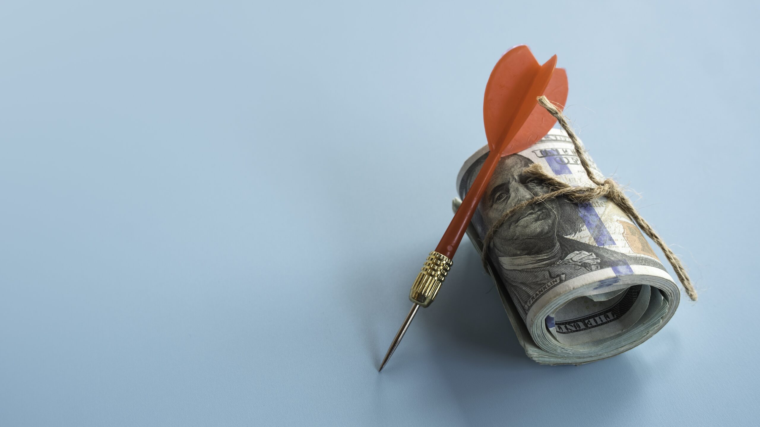 A dart pinned into a rolled stack of cash, symbolizing a targeted marketing budget.
