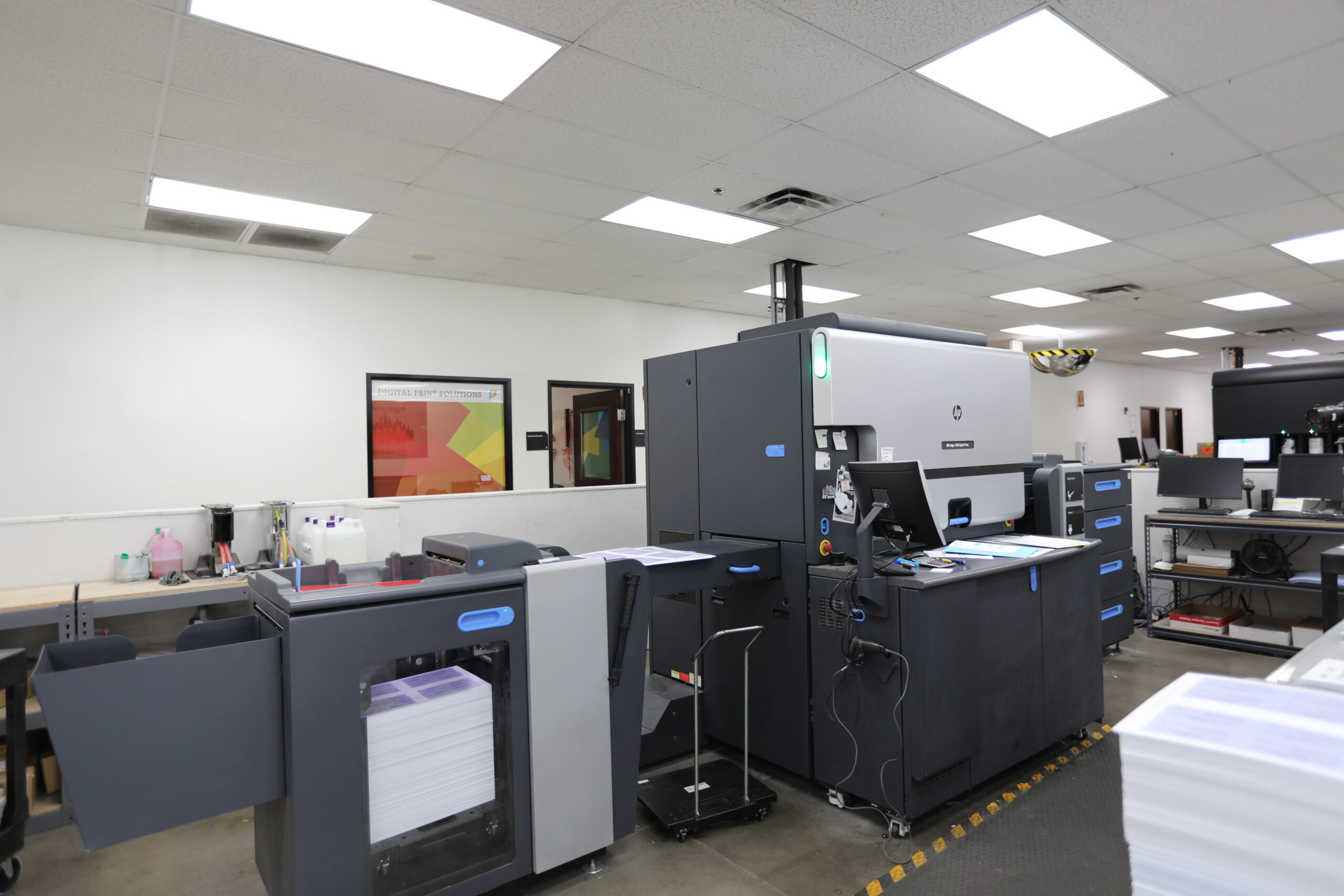 HP digital printing press on a production floor with a "Digital Print Solutions" sign in the background.