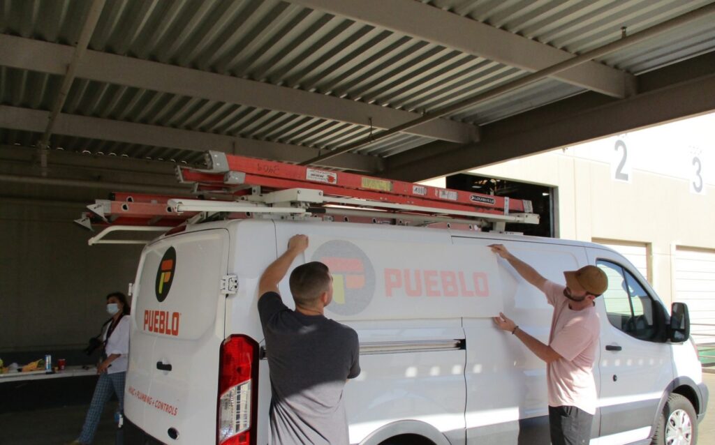 Pueblo Vehicle Wrap - Two men working on adding vinyl wrap to a van