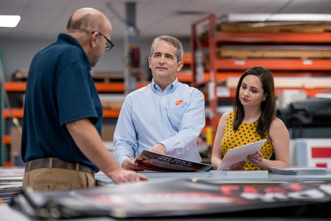 Prisma team members discussing printed materials and proofs in a production facility.