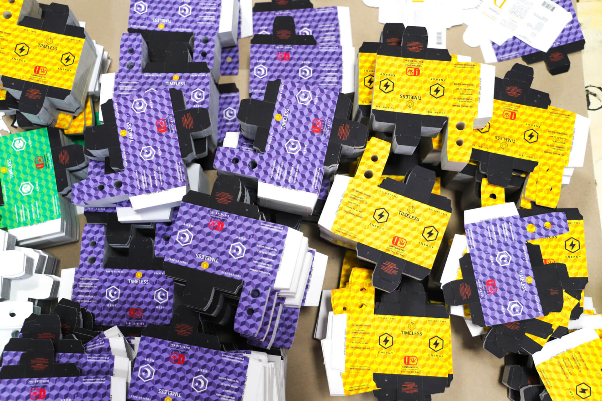 Purple and yellow custom die-cut cannabis vape packaging boxes stacked in bins.