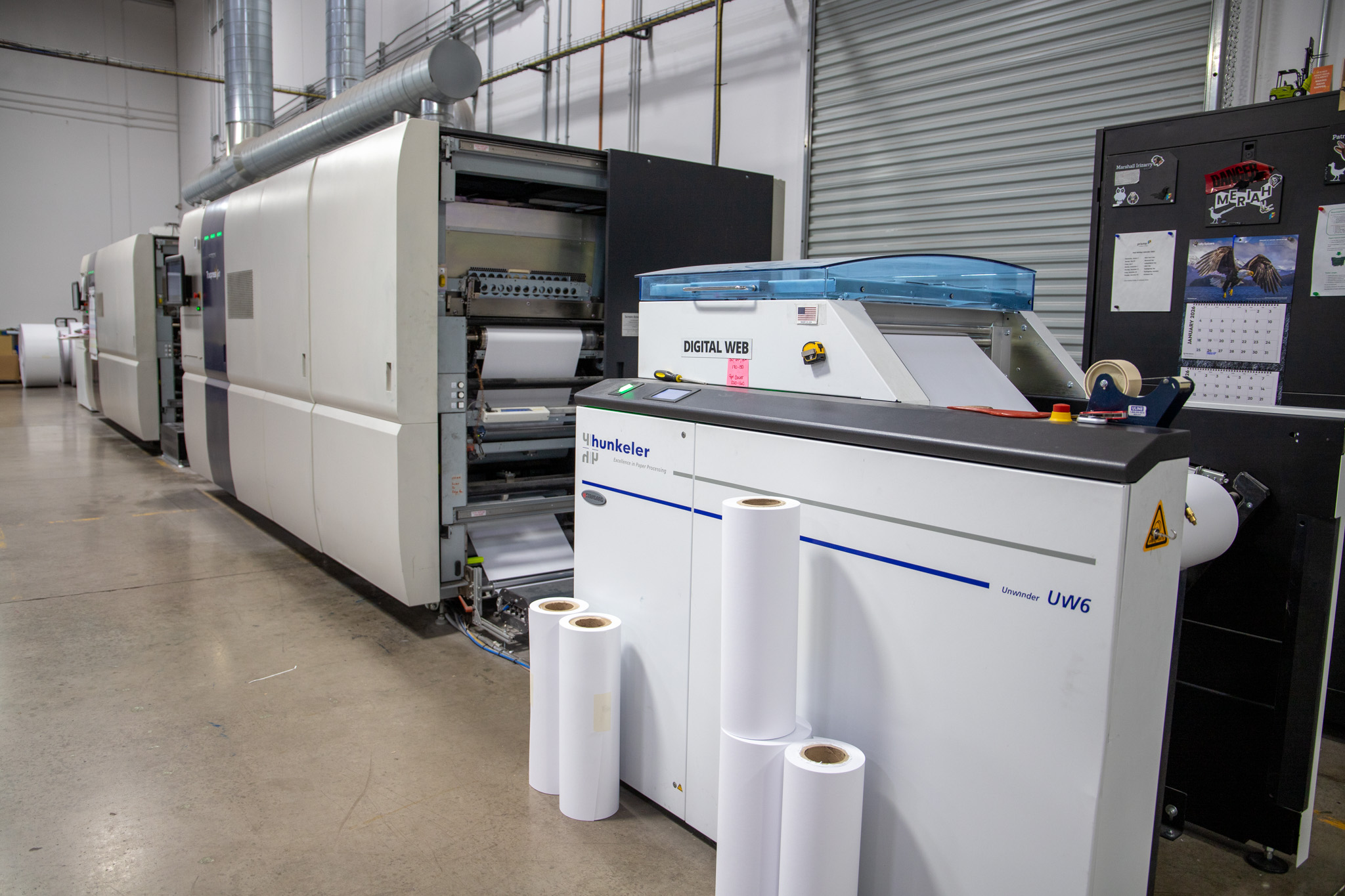 Industrial digital web press with paper rolls on the production floor.