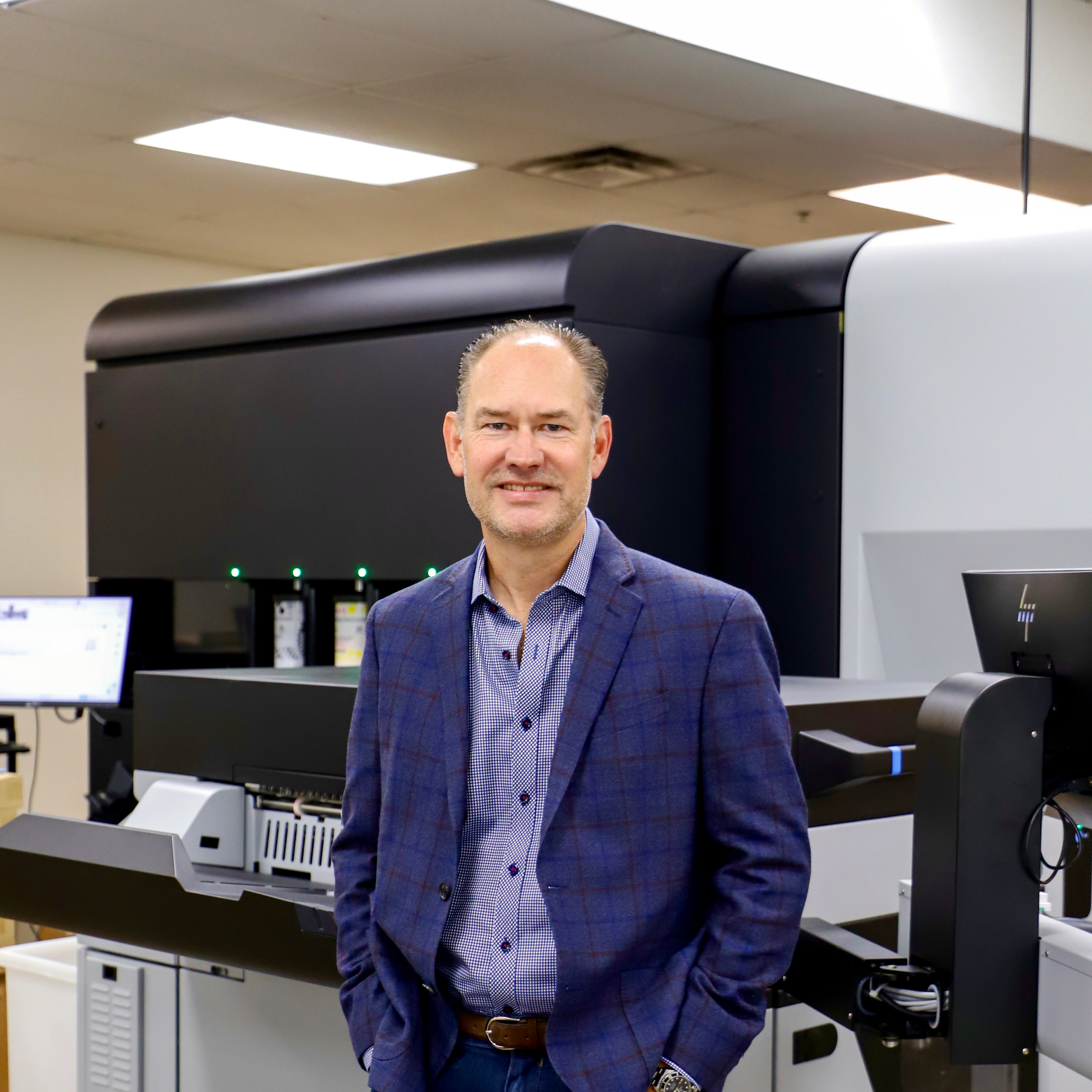 Prisma executive in a blazer standing next to a large HP digital printing press.