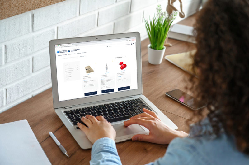 Woman browsing a branded online ordering portal on her laptop at a wooden desk.