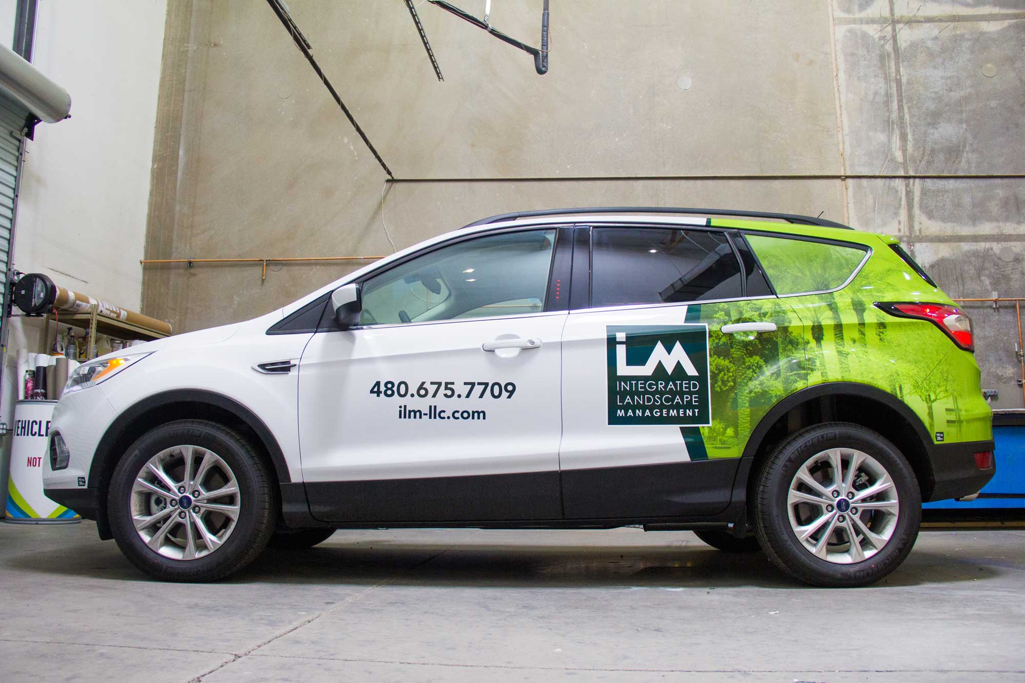White SUV with a green Integrated Landscape Management (ILM) vehicle wrap parked in a garage.