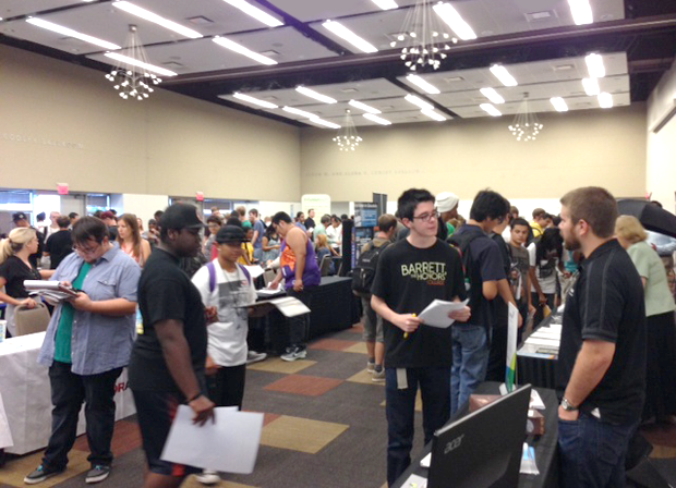 Students browsing exhibitor booths at a busy university career fair event.