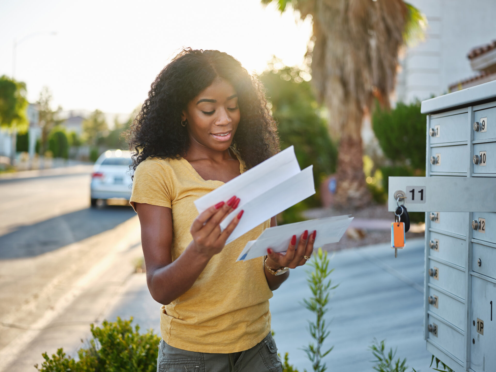 Woman smiling while reading mail she just pulled from a community mailbox.