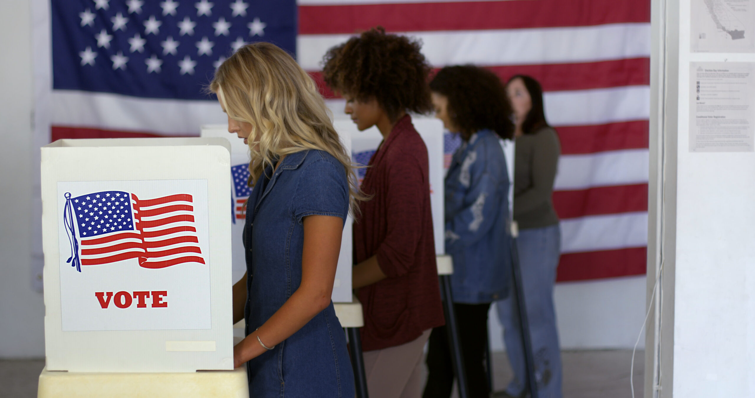 Voters casting ballots at polling booths in front of an American flag.