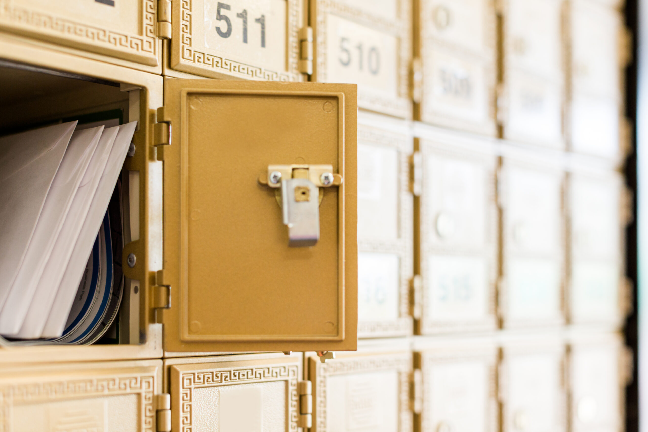Row of gold PO box mail slots with one open, showing stacked mail inside.